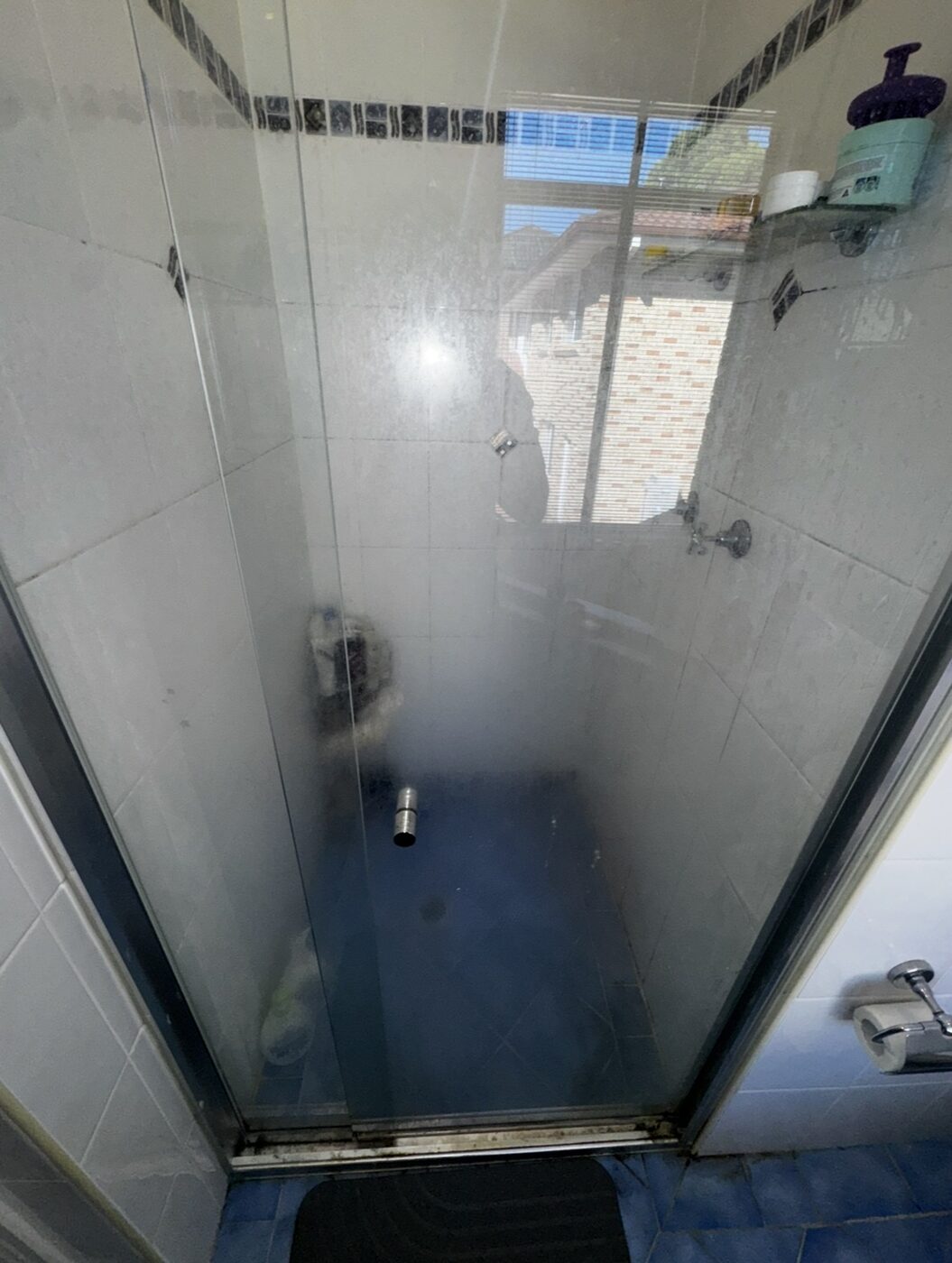 Shower glass before — heavy soap scum and hard water fogging